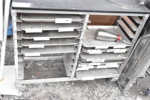 Metal commercial double pan transport rack with multiple metal baking pans, on sturdy casters. Visible labels for content organization.