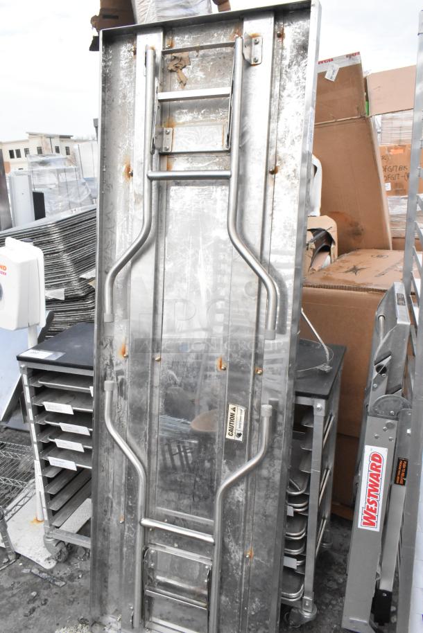 Metal folding table with visible wear and Westward ladder attachment. Folding mechanism visible; caution label intact.