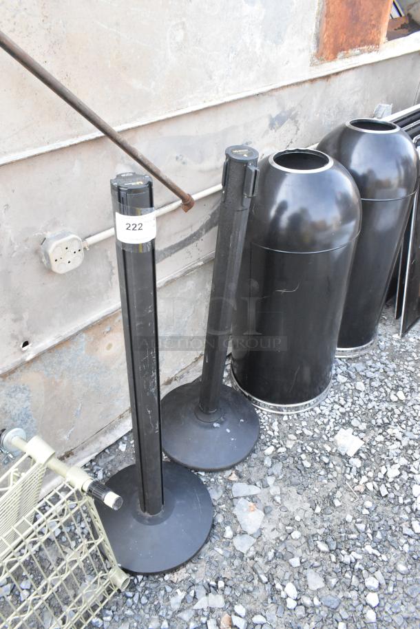 Two black stanchions and two black metal trash can shells, used condition, identification tag 222 visible on one stanchion.