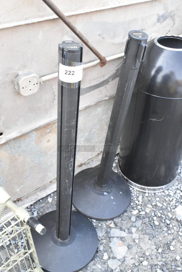 Two black stanchions with base and label "222," alongside two black metal trash can shells, showing moderate wear.