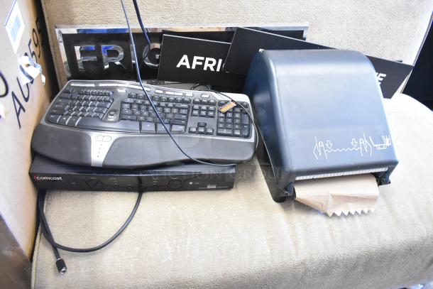 Auction lot with mixed items: paper towel dispenser, keyboard, trash can, Comcast device. Used condition, assorted labels visible.