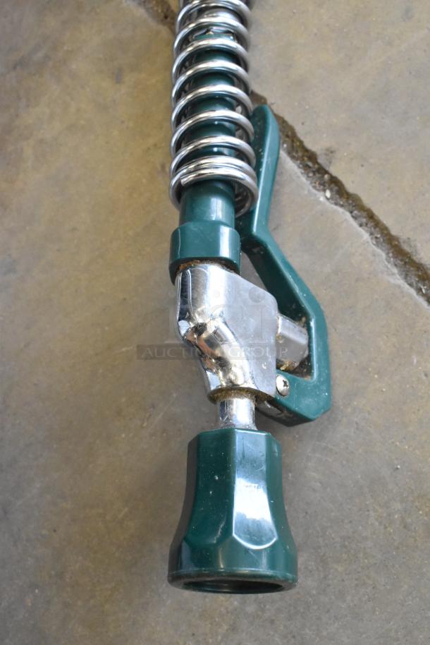 Metal faucet with spray nozzle, green and silver finish, coiled design. Slight wear visible, industrial style.