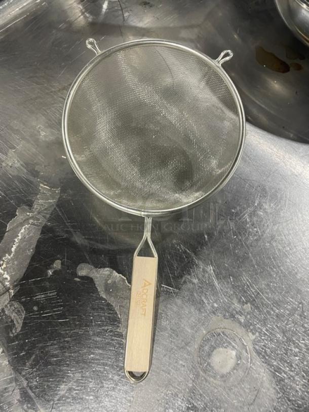 Adcraft stainless steel heavy-duty strainer with hardwood handle, featuring fine mesh design. Brand logo visible on handle.