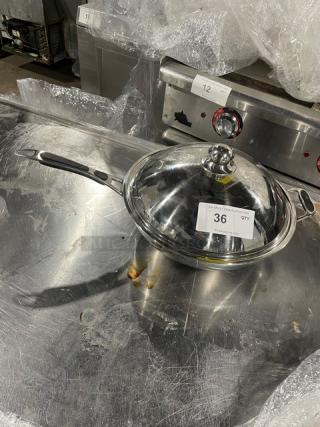 Commercial stainless steel kitchen pan with lid, featuring gray grip handle. Appears in used condition, auction tag "36."