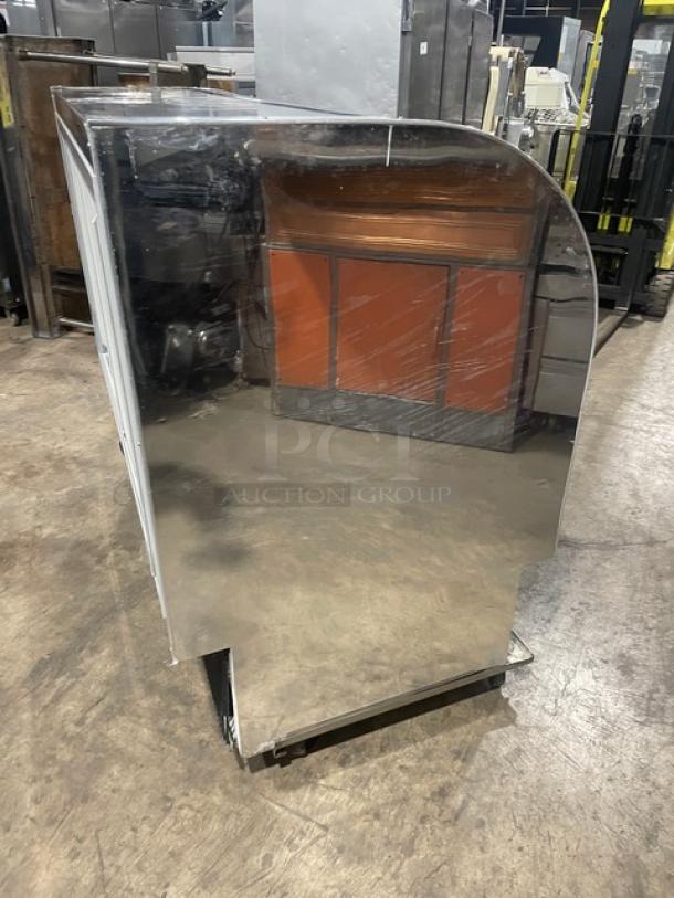 Marc stainless steel curved glass refrigerated bakery display case, poly coated wire rack, rear sliding doors, on casters.
