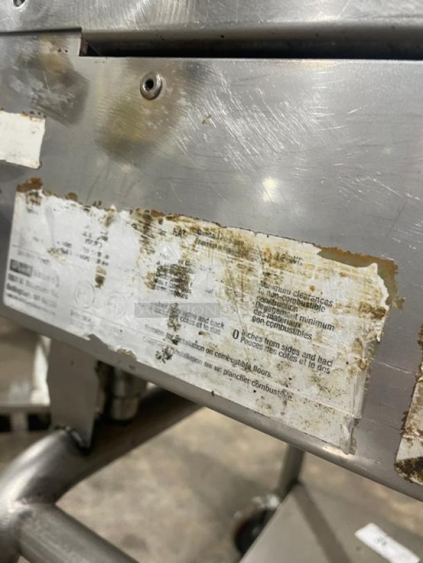 WoodStone stainless steel natural gas countertop plancha griddle with back/side splash, undershelf cart on casters, worn label.