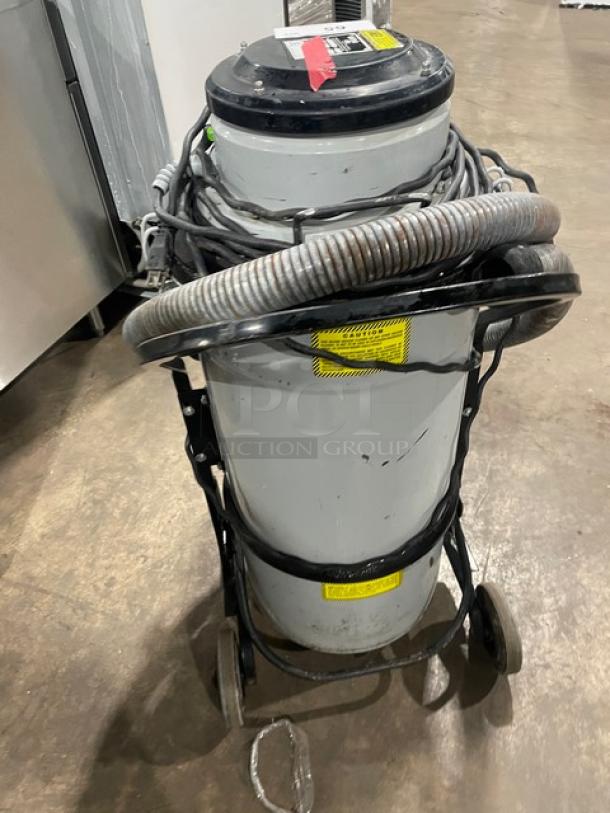 Nilfisk CFM Model 118 industrial vacuum cleaner, 120V, on casters. Features include electric power, SN: 15A1634. Visible hose and caution labels.