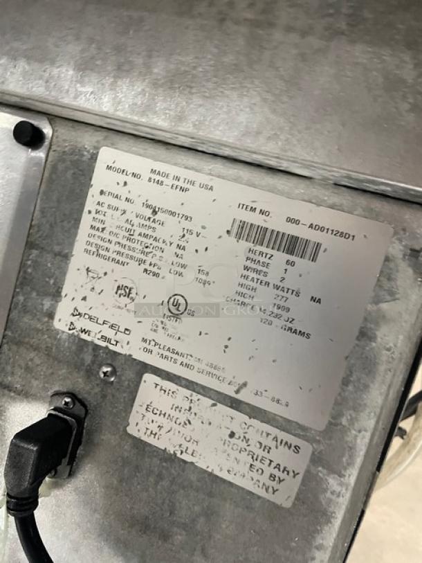 Delfield stainless steel refrigerated drop-in cold food table model 8148EFNP, serial number 1904150001793. Features include electric power, narrow 2-well design, single undershelf, and 115V 1-phase operation. Image shows product labels with technical details.