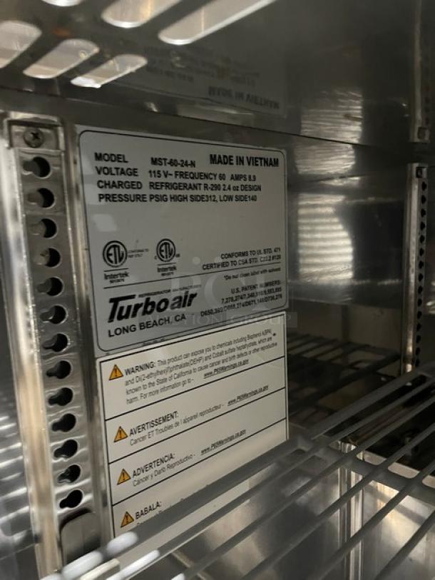 Turbo Air MST-60-24-N refrigerated prep table, stainless steel, 2-door, poly-coated rack, 115V, on casters, label showing specs.