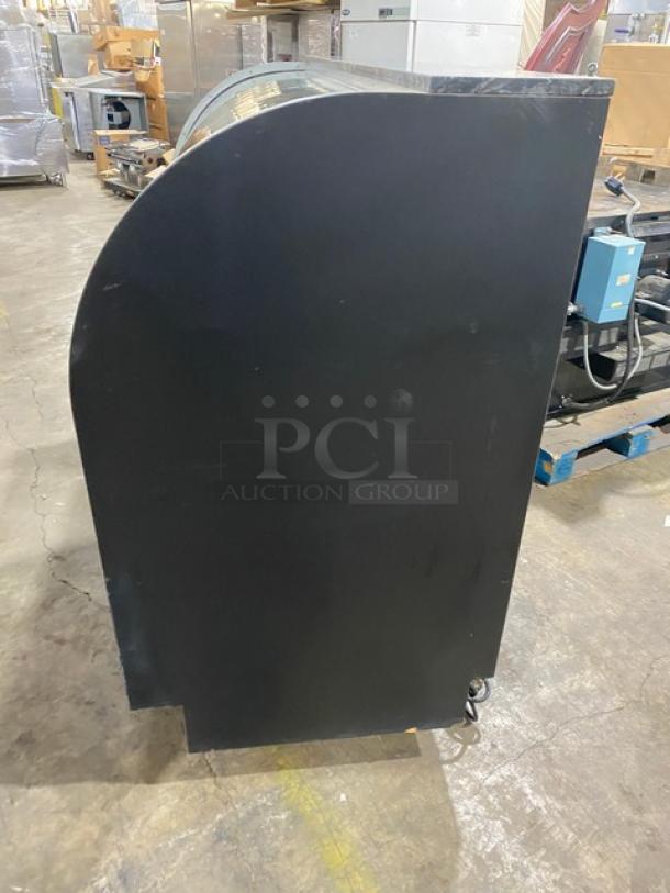 Commercial black curved glass bakery display case with multi-tier shelves, lower storage, rear sliding doors. Used condition.