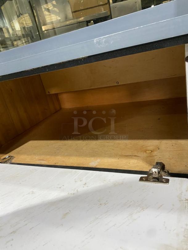 Commercial black curved glass bakery display case with multi-tier shelving, rear sliding doors, and overstock compartment.