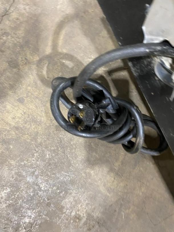 Coiled electrical cord on a commercial bakery display case, set on a concrete floor, showing plug details.