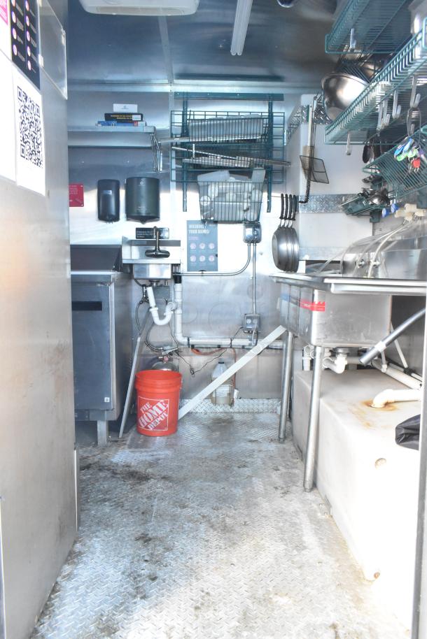 Interior of a Cruising Kitchens 24' food trailer with commercial equipment, stainless steel sink, and storage shelves.