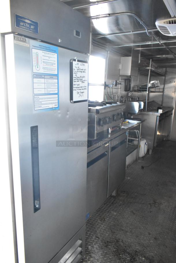 Interior of 24' Cruising Kitchens food trailer featuring Arctic Air freezer, commercial stove, and prep area. Clean condition.