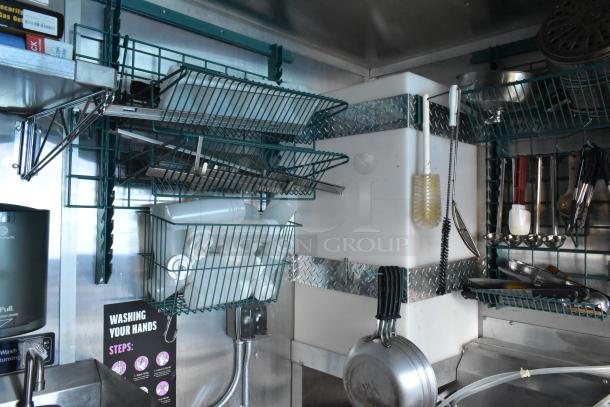 Interior of a Cruising Kitchens 24' unbranded food trailer, showing wire racks, utensils, and a handwashing station.