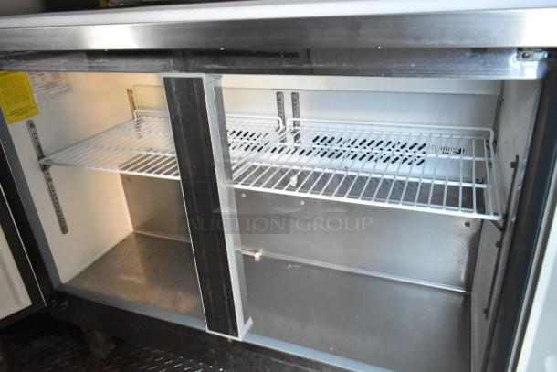 Interior view of an Arctic Air undercounter cooler/freezer in a Cruising Kitchens 24' food trailer, featuring wire shelving and stainless steel finish, showing ample storage space.