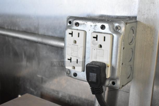 Electrical outlet inside a Cruising Kitchens food trailer, featuring a mounted dual socket with a GFCI outlet and plugged-in black cord.