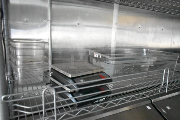 Stainless steel shelving with scales and clear storage containers in a food trailer kitchen. Commercial setup for efficient food prep.