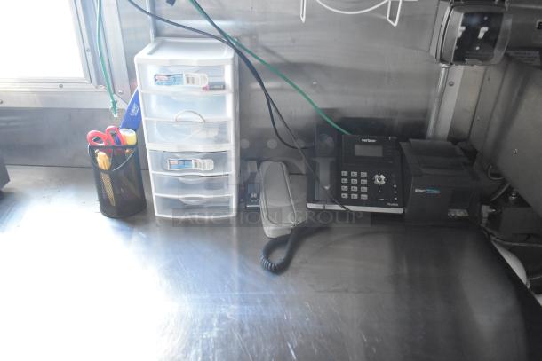 Interior of a 2021 Cruising Kitchens 24' food trailer, featuring a phone system, storage drawers, and organizer with utensils.