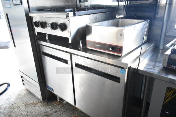 Brand new Cruising Kitchens 24' food trailer interior, featuring Wells range, Winco warmer, Arctic Air coolers, and stainless fixtures.