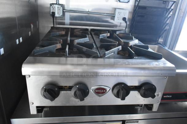 "Wells four-burner range inside a Cruising Kitchens food trailer, featuring stainless steel knobs and commercial-grade finish."