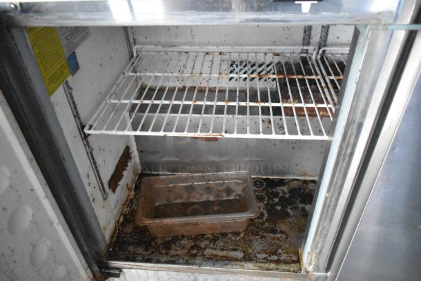 Interior view of an empty and rusted undercounter refrigerator interior with wire shelving, showing signs of wear and potential need for cleaning or restoration.