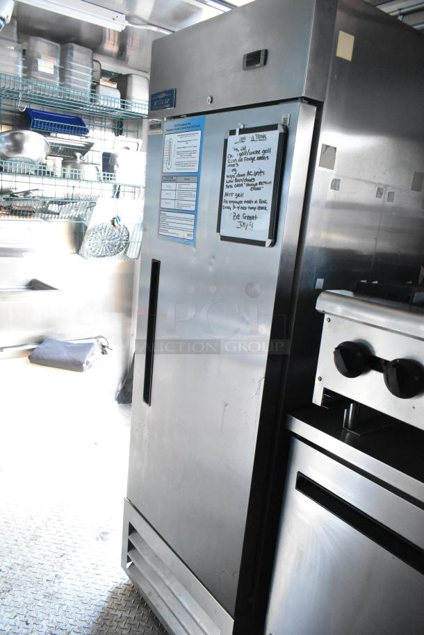 Cruising Kitchens food trailer interior, featuring Arctic Air cooler with attached clipboard, stainless steel finish, shelving above.