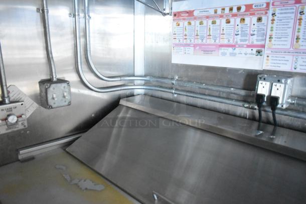 Interior of Cruising Kitchens 24' mobile food trailer, showing stainless steel surfaces, electrical outlets, and a menu display.