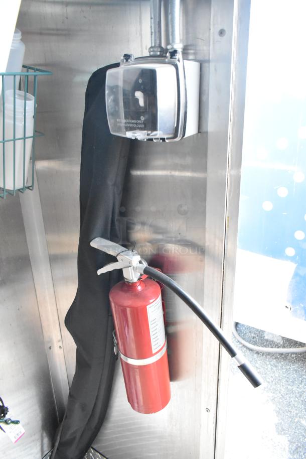 Red fire extinguisher mounted inside Cruising Kitchens food trailer; part of safety equipment.