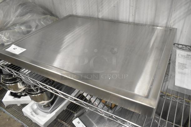 ```plaintext
Brand new stainless steel tabletop with under shelf and legs, pristine condition, auction tag "42" visible.
```