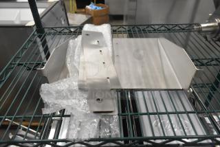 Brand new metal pieces on a wire shelf, partially wrapped in bubble wrap. Appears sturdy and clean for industrial use.