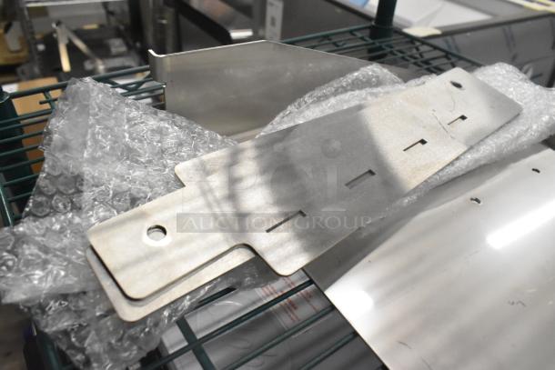 Brand new metal pieces, two units, packaged in bubble wrap on a rack. Smooth surface with cutouts for mounting.