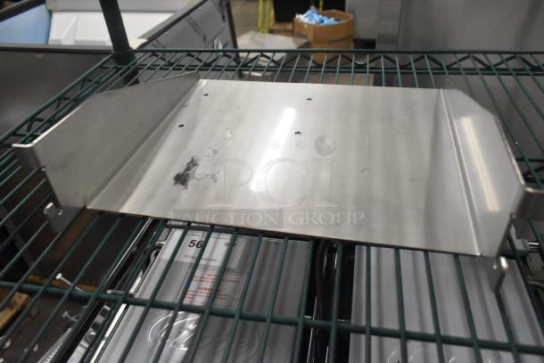 Brand new metal piece, shiny finish, with holes for mounting, stored on a green wire shelf. Auction tag visible underneath.