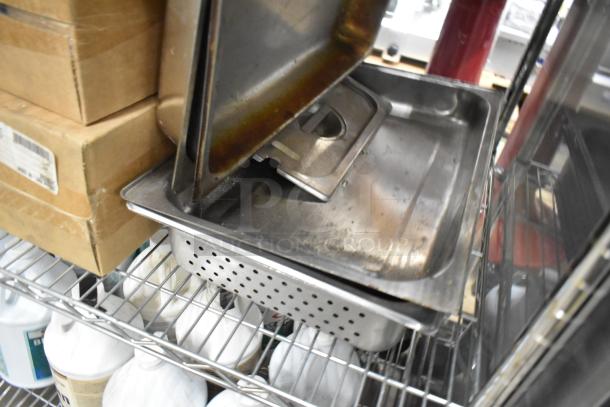 5 metal items including a steam pan, perforated drop-in, and chafer lids. Used condition, stacked on a shelf.