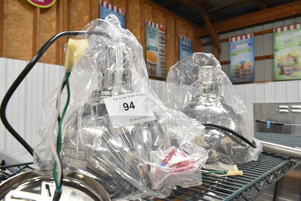 Two brand new Hatco DL-725-CN metal heat lamps, wrapped in plastic, 120 volts, 1 phase, on auction shelf.