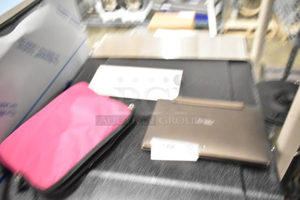 Blurry image of an Asus laptop with white keyboard and a pink case, on a display table.