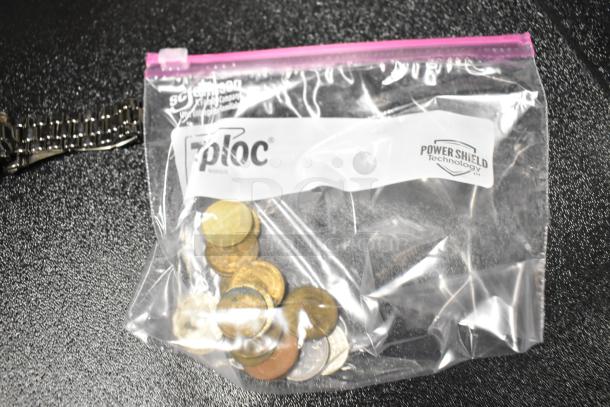 Bag of assorted coins next to a watch with metal strap on black surface. Ziploc bag labeled with “Power Shield Technology.”
