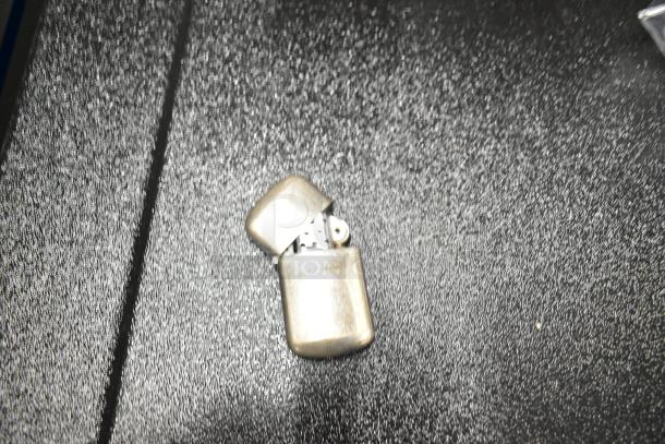 Silver metal lighter with hinged lid, shown open. Surface shows wear, suggesting use. No visible brand markings.