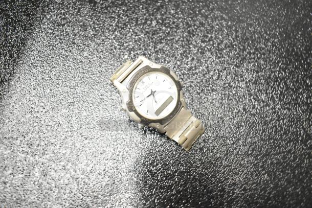 Silver wristwatch with white dial on a textured black surface. Quartz movement, metal band, and visible brand label.
