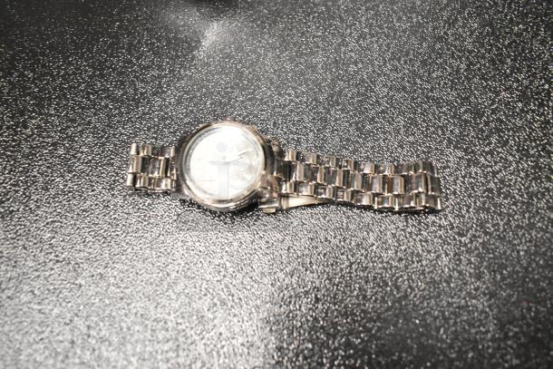 Silver metal wristwatch with linked bracelet in used condition on textured surface. Part of a mixed lot auction.