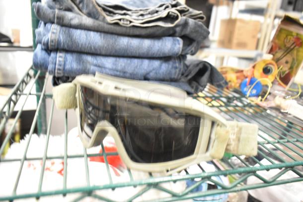 Mixed lot including folded jeans, protective goggles, and toys on a metal shelf. Items appear used.