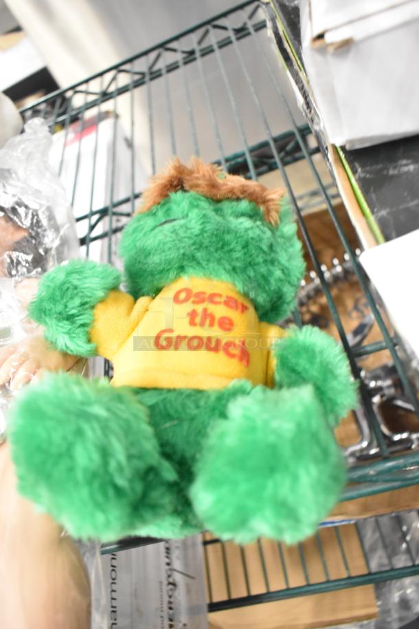 Green Oscar the Grouch plush with "Oscar the Grouch" on yellow shirt, part of a 6-stuffed animal auction set.