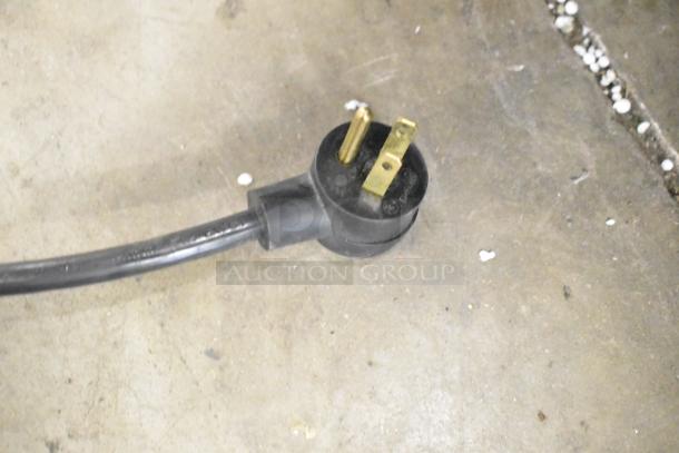 Close-up of a power plug for the 2019 Habco SE18 commercial cooler, showing a three-prong design on a concrete floor.