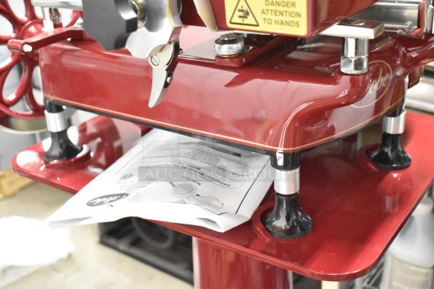 BRAND NEW Globe FS12 metal meat slicer with flywheel, blade sharpener, and manufacturer’s manual underneath.