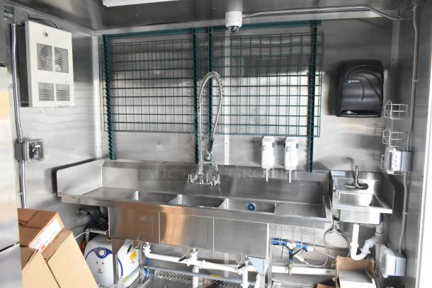 Commercial kitchen sink area inside Cruising Kitchens 24' trailer, featuring a stainless steel triple sink and soap dispensers.