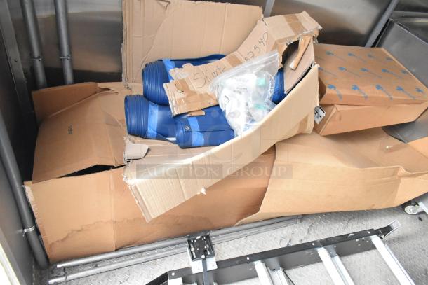 Damaged cardboard boxes containing blue rolled materials and various smaller items inside a mobile kitchen trailer.