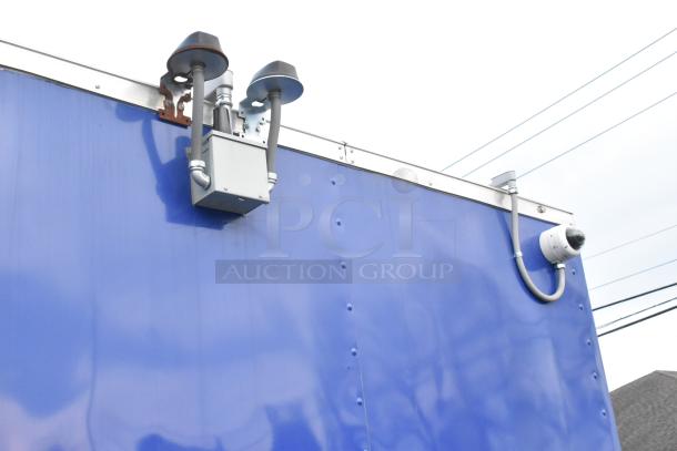 Blue exterior of a 2021 Cruising Kitchens 24' fast food trailer with mounted security cameras and equipment.