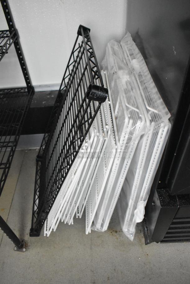 Multiple metal shelves, black and white, leaning against a wall in a retail trailer setup.
