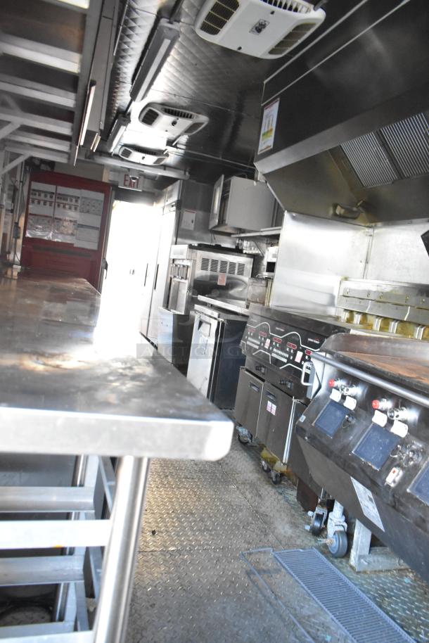 Interior of a commercial food truck featuring stainless steel countertops, ventilation hoods, and cooking appliances. Clean condition.