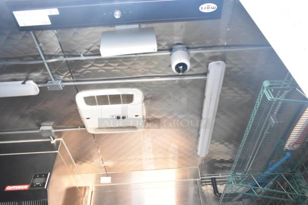 Commercial kitchen ceiling with stainless steel finish, featuring HVAC unit, surveillance camera, fluorescent light, and shelving.